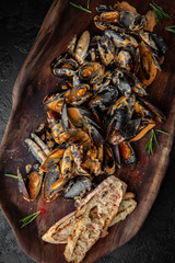 Delicious cooked mussels in sauce with dried baguette. Sea food serving in a wooden plateau
