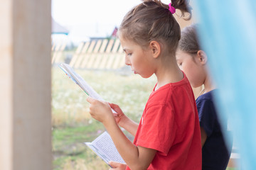 Girl enthusiastically reads a book in the backyard of a village house
