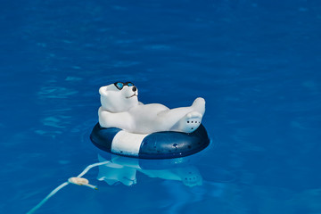 Pool decoration in the form of a relaxed bathing polar bear with sunglasses and a swim ring on blue...