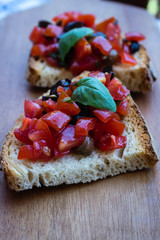 Tasty tomato italian bruschetta on toasted slices of bread seasoned with spices and herbs garnished with fresh basil on a wooden board. Selective focus 