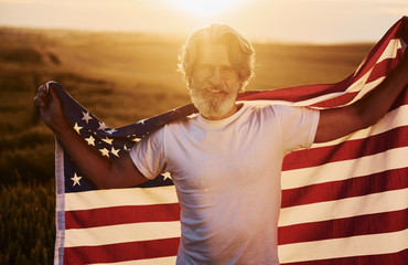 Conception of freedom. Holding USA flag. Senior stylish man with grey hair and beard on the agricultural field with harvest