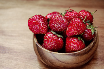 Macro photo of red fresh and sweet strawberries in wooden bowl at light wooden background.