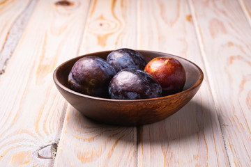 Obraz premium Fresh sweet plum fruits in brown wooden bowl, wood table background, angle view