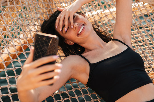 Image of girl taking selfie photo on cellphone while lying in hammock