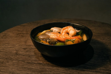 Thai Spicy Mixed Vegetable Soup with Prawns (Gang Liang) on black black bowl wooden table isolated on Dark Slate Gray Concrete Wall background