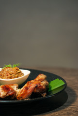 Thai grilled chicken wing on bamboo leave with traditional Thai blend of Fermented fish spicy dip on black plate isolated on Dark Slate Gray Concrete Wall background
