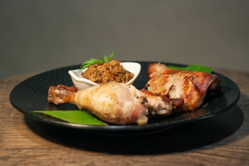 Thai grilled chicken wing on bamboo leave with traditional Thai blend of Fermented fish spicy dip on black plate isolated on Dark Slate Gray Concrete Wall background