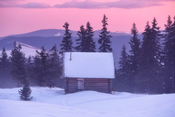 Old wooden hut on the lawn covered with snow. Fantastic sunrise. Majestic winter scenery. Landscape of high mountains and forests. Wallpaper background. Location place Carpathian, Ukraine, Europe.