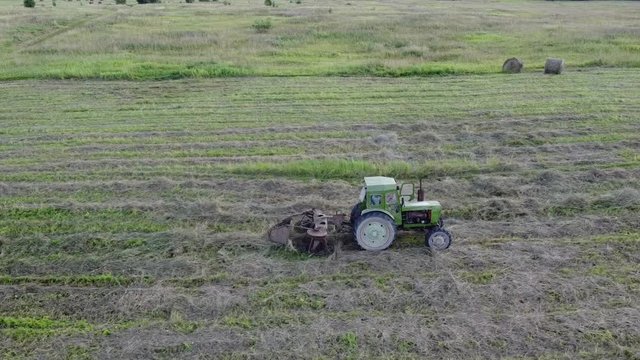 tractor with tedder collects hay in one line