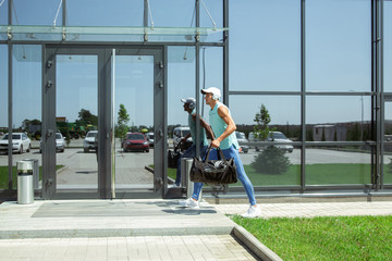 Fototapeta premium On the way. Sportsman walking down against modern glassed building, airport in megapolis. Before flight to competition. Professional stylish, confident athlete. Journey, vacation, sport lifestyle.