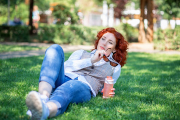 Fototapeta premium A cute red-haired girl lies in the park on the grass and thinks or dreams about something.