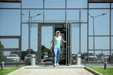 Sportsman walking down against modern glassed building, airport in megapolis in summer's day. Before flight to competition. Professional stylish, confident athlete. Journey, vacation, sport lifestyle.