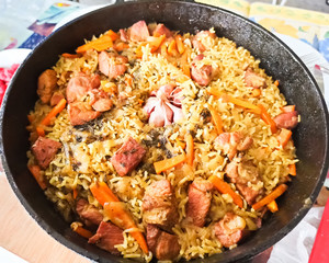 Close-up delicious pilaf in a cauldron. Appetizing Uzbek pilaf from rice and pork. Head of garlic on rice. Central-Asian cuisine - Plov Top view.
