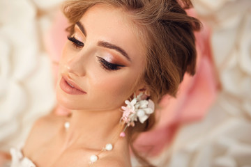 Beautiful young bride with makeup and fashion wedding hairstyle. Closeup portrait of young gorgeous woman over roses flowers. Studio shot.