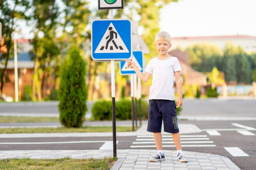 a child stands at a Pedestrian crossing sign and points at it with his finger, traffic rules for children