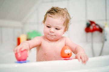 Cute adorable baby girl taking foamy bath in bathtub. Toddler playing with bath rubber toys....