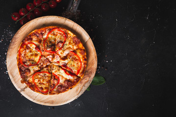 Overhead shot of Italian pizza on the wooden plate with bazil, tomatoes and salt scattered on the black background with copy space