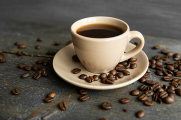 Coffee cup with roasted coffee beans on wooden table background. Mug of black coffe with scattered...