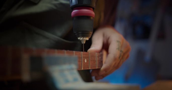 Close up of male hands with tattoos drilling thin screw in wooden guitar neck professional, artisan joiner specialist construction using tools for wooden planks details, hobby art concept in workshop