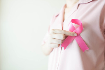 Breast Cancer Awareness Month in October. Close up of woman in pink shirt showing satin pink ribbon awareness for support people who live w/ breast cancer. Health care and medical concept. Copy space.