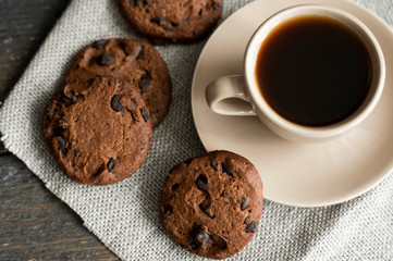 Coffee cup with cookies and chocolate on wooden table background. Mug of black coffee with chocolate cookies. Fresh coffee beans.