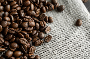 Coffee beans on a linen textile and on a wooden table background. Fresh arabica coffee beans.