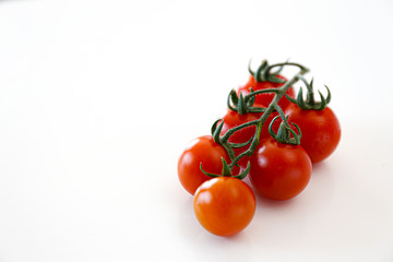 Branch of beautiful juicy organic red cherry tomatoes on white background. Top view of shiny polished glossy vegetables. Clean eating concept. Vegetarian vegan summer detox diet. Copy space, flat lay.