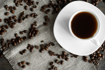 Coffee cup with roasted coffee beans on wooden table background. Mug of black coffe with scattered...