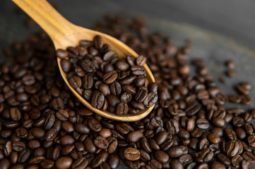 Fresh roasted arabica coffee beans in a wooden spoon and scattered coffee beans on a wooden table.