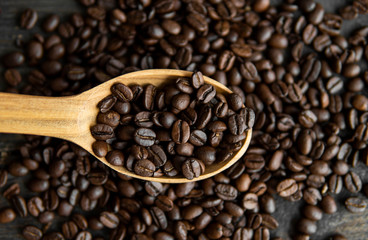 Fresh roasted arabica coffee beans in a wooden spoon and scattered coffee beans on a wooden table.