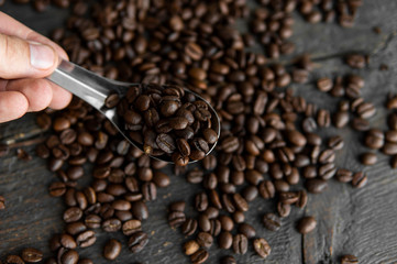 Fresh roasted arabica coffee beans in a metal spoon and scattered coffee beans on a wooden table.