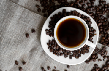 Coffee cup with roasted coffee beans on linen background. Mug of black coffe with scattered coffee beans. Fresh coffee beans.