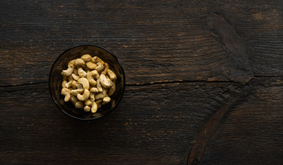 Obraz na płótnie Canvas Cashew nuts in a small plate on a vintage wooden table as a background. Cashew nut is a healthy vegetarian protein nutritious food.