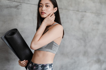 Image of beautiful asian girl in sportswear posing with yoga mat