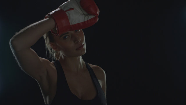 Exhausted woman boxer wiping sweat from face after sport workout in black studio