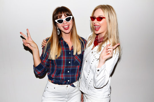 Trendy hipster happy two best friends girls having fun together showing ok science, white background, flash image, American vintage retro style. Students enjoying party.
