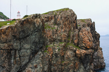Lighthouse, huge rocks on the ocean, sea summer landscape, old stone building on a high cliff,...
