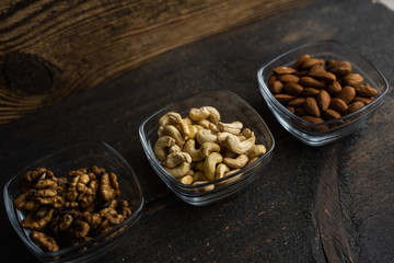Almond, cachew and walnut in a small plates which standing on a black table. Nuts is a healthy vegetarian protein and nutritious food.