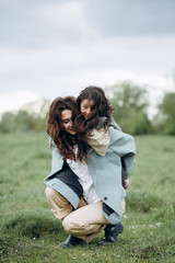 Fototapeta premium Portrait of hipster mother with daughter in her arms in the field. The family is having fun together