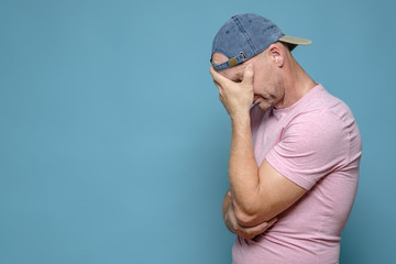 Man in the cap and t-shirt was very tired, upset and stressed, covered face with hand and bowed...