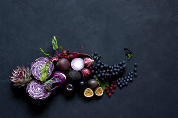 Composition of Vegetables, fruits and berries purple on a black background. cabbage, kohlrabi, artichoke, passion fruit, avocado, beetroot, grapes, onion, garlic, plum.