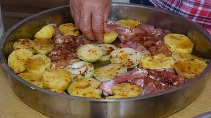 Female hands preparing pan with potatoes, onion and chicken.