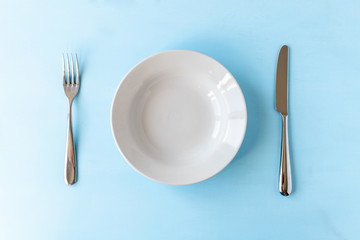 empty plate, knife and fork on light blue background
