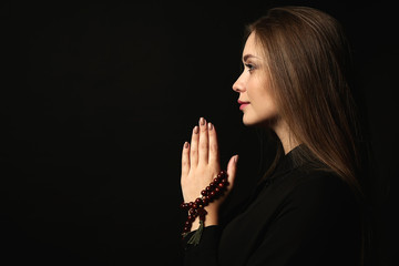 Beautiful young woman praying on dark background