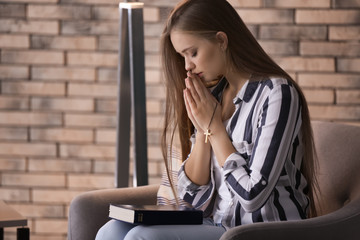 Beautiful young woman praying at home