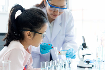 Asian children analyzing study evaluating microscope with scientist. Health care researchers doing some research with dropper chemical testing 