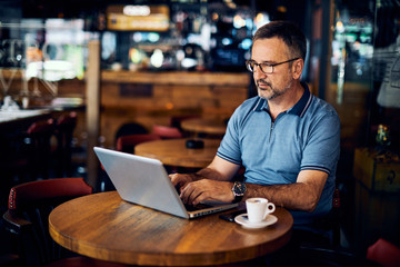 Mature adult man sitting in cafeteria and typing on laptop.