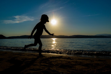 Happy Toddler Silhouette Running On The Beach At Beautiful Sunset, in Greece, Skiathos