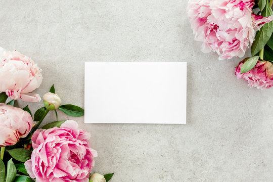Mockup invitation, blank paper greeting card and peonies on gray stone table. Flower background. Flat lay, top view.