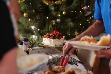 Pavlova with cream & berries – Australian dessert. Christmas family buffet lunch with Christmas tree with lights and baubles.